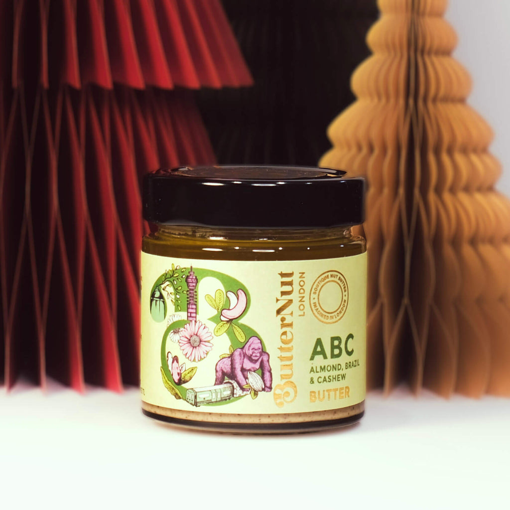 Red, green, and golden paper trees with a jar of ButterNut of London ABC (Almond, Brazil) Butter on a white background.