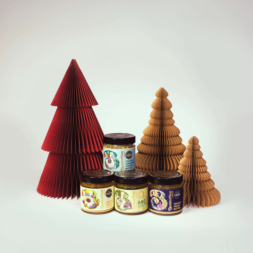 Red and golden paper trees with jars of ButterNut of London Nut Butters on a white background.