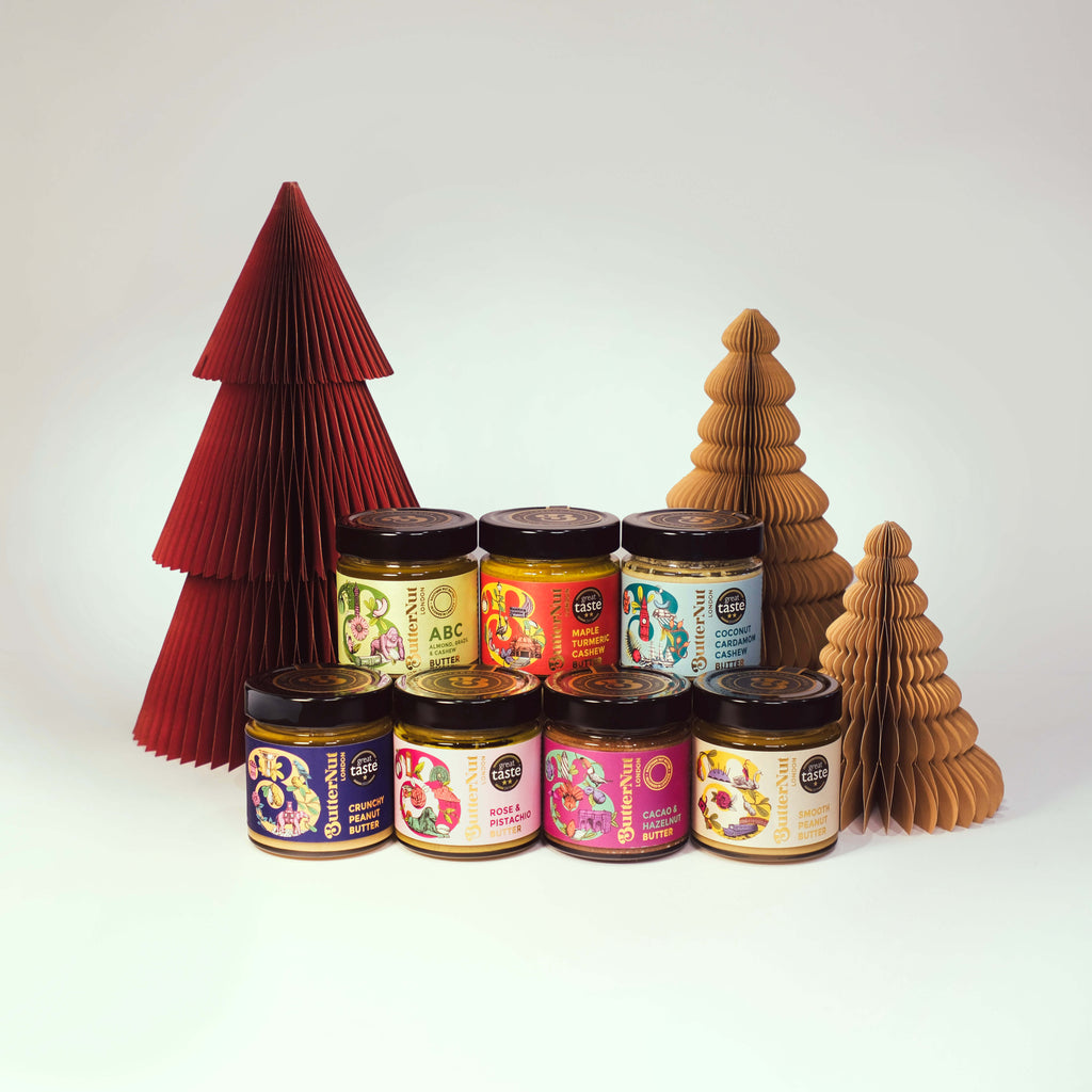 Red and golden paper trees with the full range of jars of ButterNut of London Nut Butters on a white background.